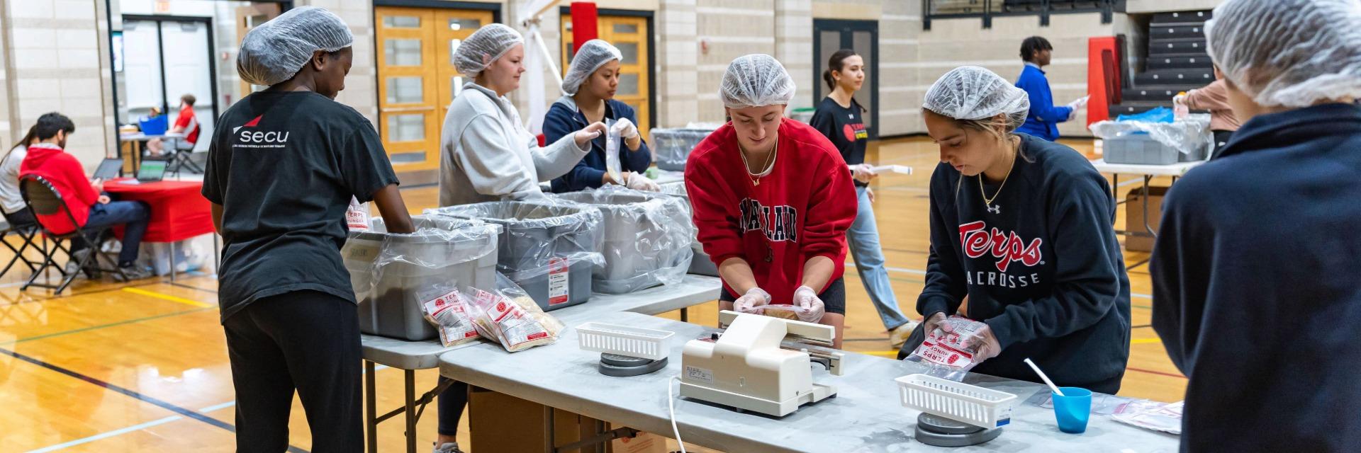 Six University of Maryland Students wearing hair nets package food for the Terps Against Hunger food packaging event in Ritchie Coliseum.